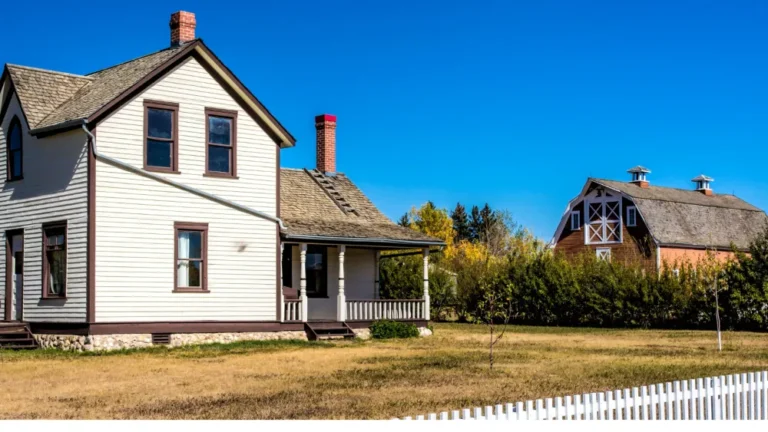 An older white farmhouse with a red barn and a white picket fence