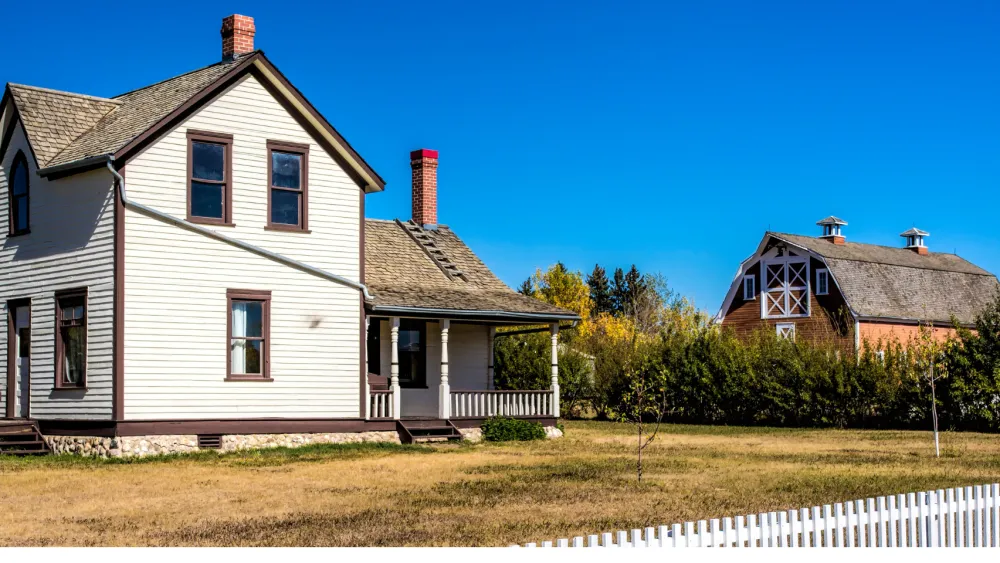 An older white farmhouse with a red barn and a white picket fence