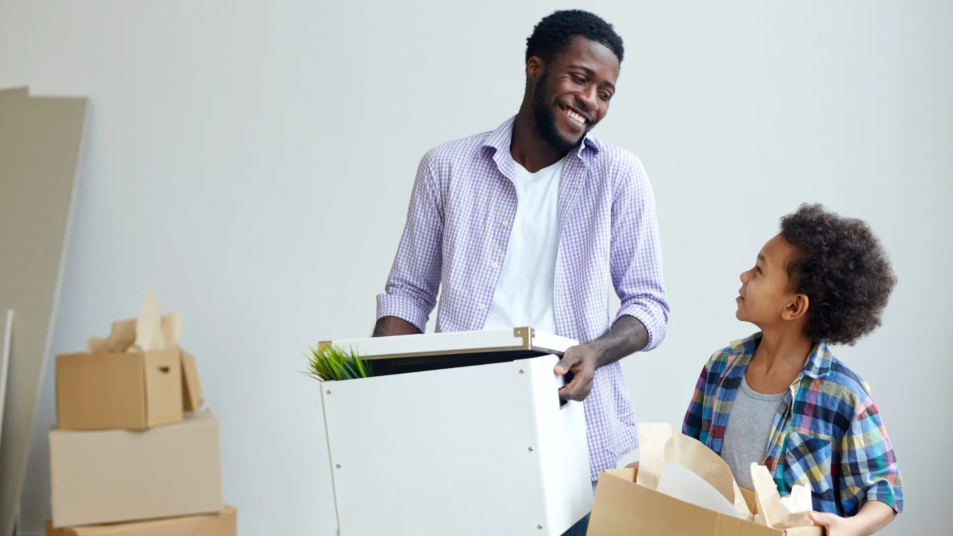 Smiling father and son carrying moving boxes into their new home